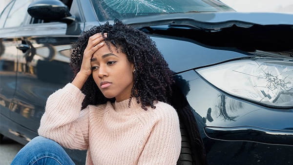 Woman In Car Accident Sitting Next To Her Car With Hand On Forehead